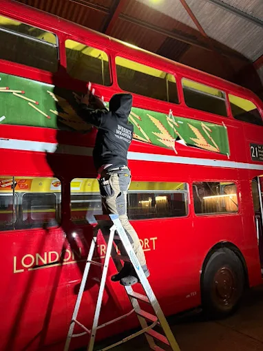 A Wessex Wrapping fitter applying vinyl to a classic red London Routemaster bus